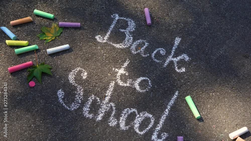 Closeup top view of phrase Back to school drawn with white chalk on grey surface of sidewalk. Zooming. Real time 4k video footage.