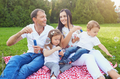 Happy family has fun playing with soap bubbles on the grass in the park. © Studio Romantic