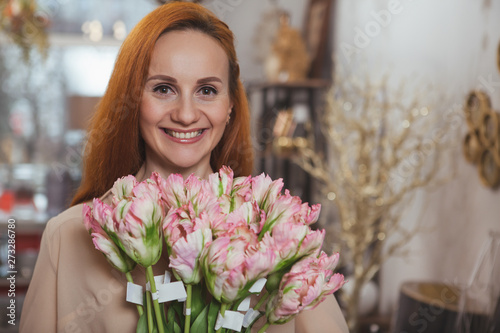 Happy mature woman smiling cheerfully to the camera, holding bunch of beautiful flowers at flower shop, copy space. Excited mature woman buying flowers at homeware store. Happiness, femininity concept photo
