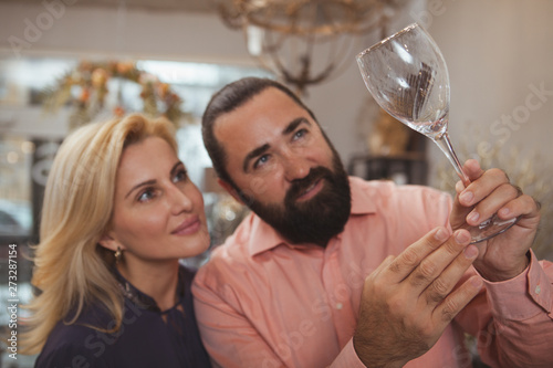Close up of a mature lovely couple examining wine glass while shopping at homegoods store, copy space. Beautiful woman and her bearded handsome man buying wine glasses together, selective focus photo