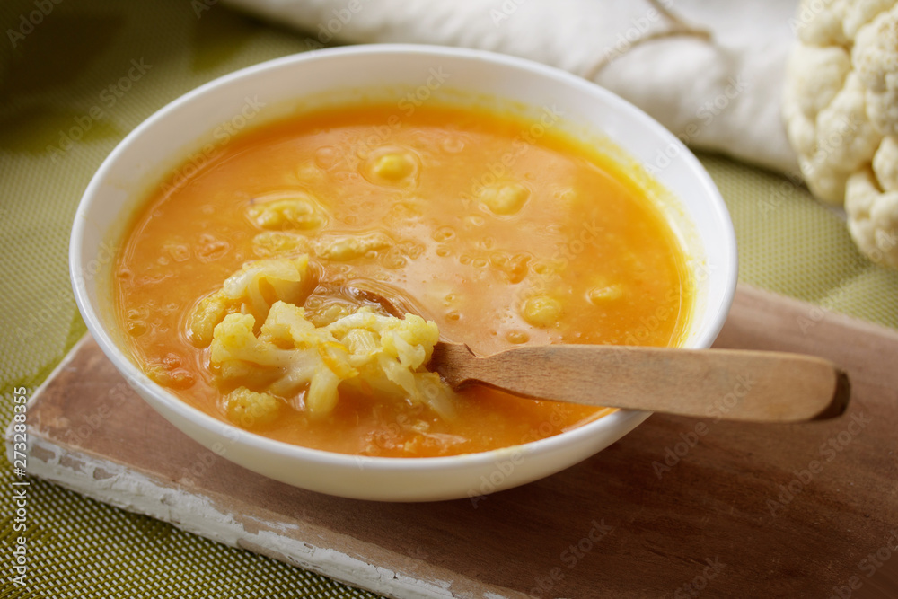 Roasted pumpkin and carrot soup with cauliflower on a wooden board with a spoon, close-up Roasted pumpkin and carrot soup with cauliflower on a wooden board with a spoon, close-up