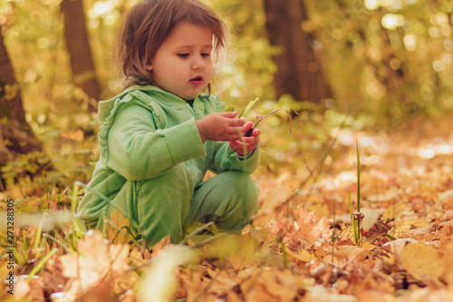 A child in a tracksuit sits and plays merrily with yellow leaves in the forest, open air, day, portrait