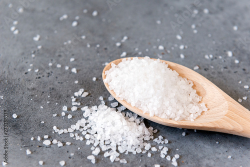 large white edible salt on wooden spoon on grey concrete background