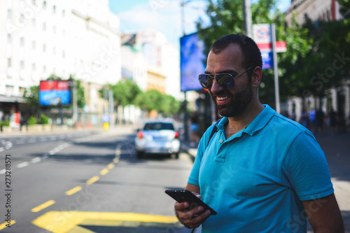 Man texting on phone. Casual urban professional entrepreneur using smartphone smiling happy outside office building. Outdoor portrait of modern young guy with mobile in the street