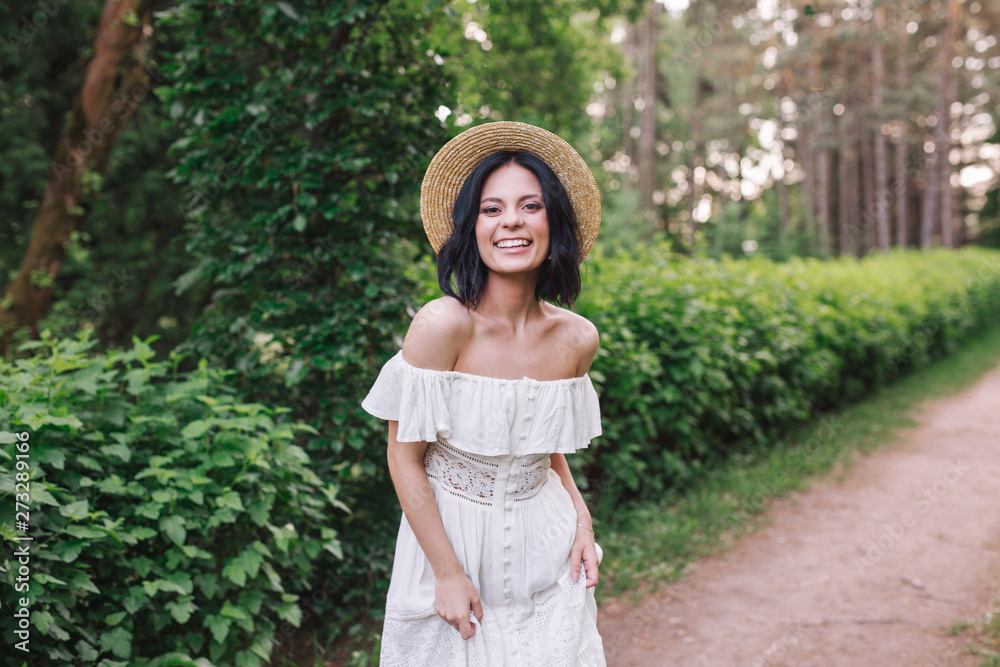 portrait of a beautiful girl in a white vintage dress and straw hat standing in park