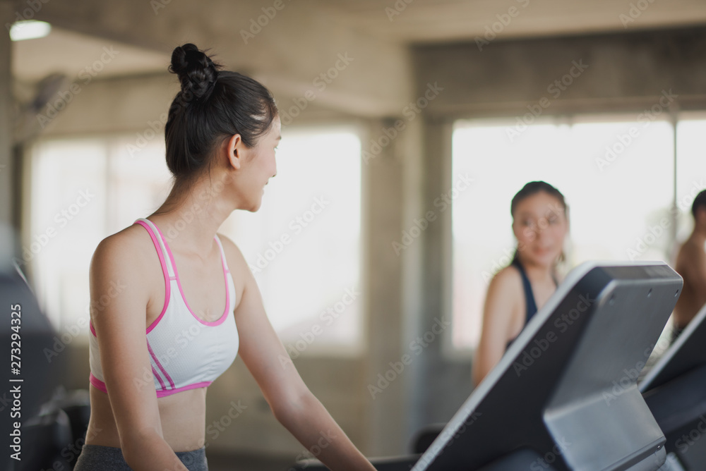 Young Asian woman walking and running on the running machine and looking her friend at the gym. Woman workout running at fitness room. People training at gym concept.