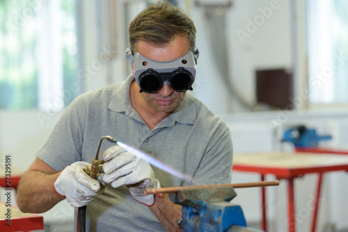 man wearing goggles while using gas torch on copper pipe