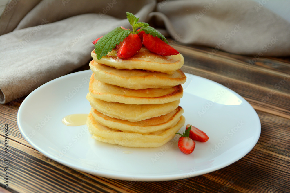 Stack of pancake with strawberries, honey and mint on a white plate Stack of pancake with strawberries, honey and mint on a white plate