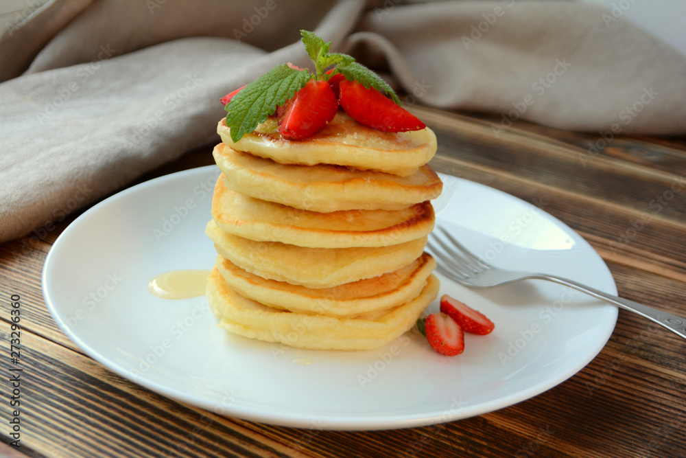 Stack of pancake with strawberries, honey and mint on a white plate