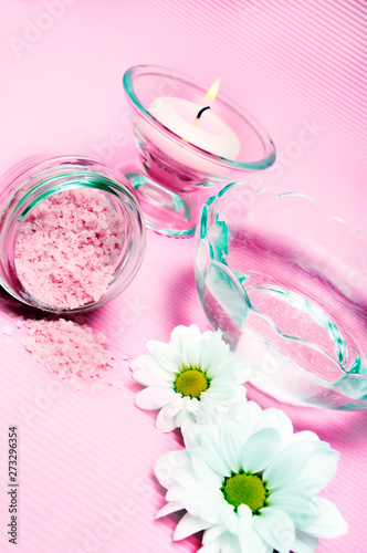 wellness, spa, body care concept with a bath salt, candle, water amd daisy flower in pink color