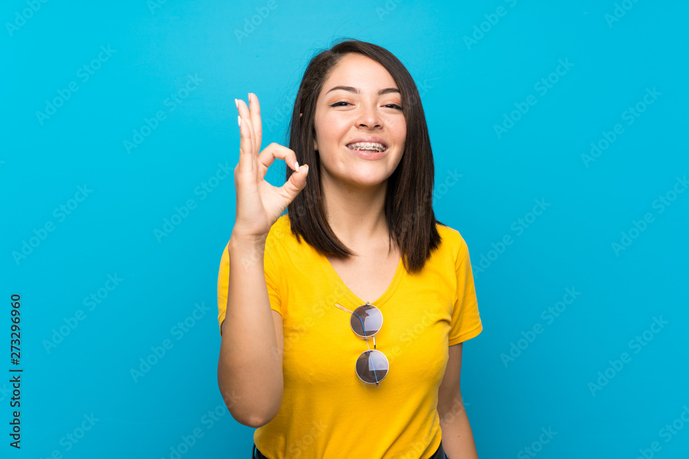 Young Mexican woman over isolated blue background showing ok sign with fingers Young Mexican woman over isolated blue background showing ok sign with fingers