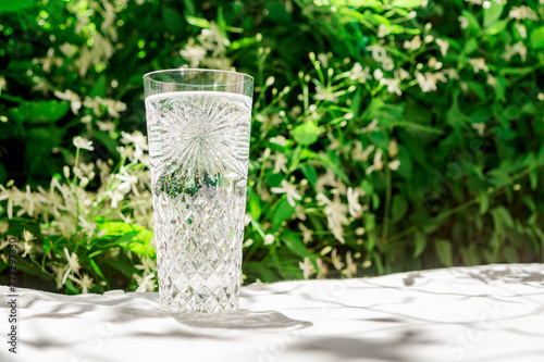 A glass of clean water with bubbles stands on a table with a white cloth against the background of blurred flowers. Copy space for your text. The concept of water and a healthy lifestyle