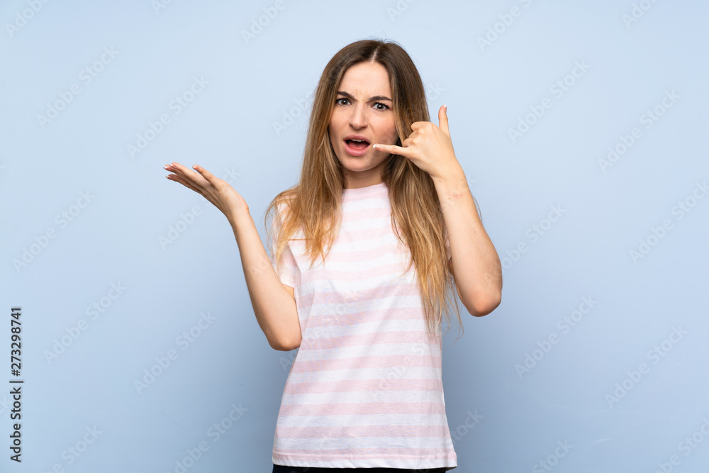 Fototapeta premium Young woman over isolated blue background making phone gesture and doubting