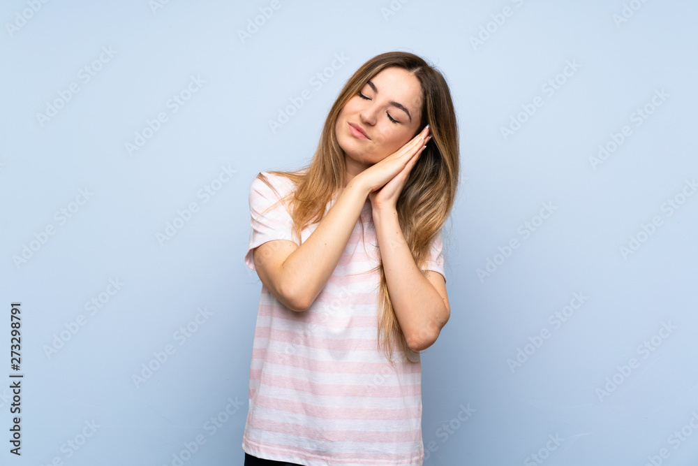 Young woman over isolated blue background making sleep gesture in dorable expression Young woman over isolated blue background making sleep gesture in dorable expression