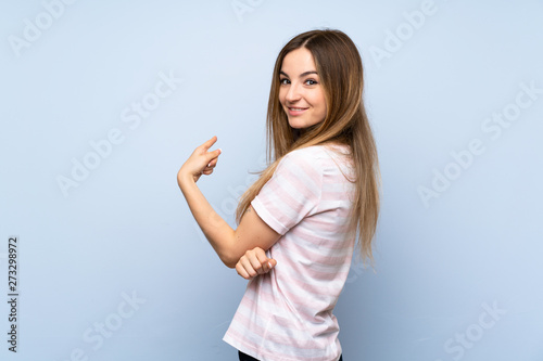 Young woman over isolated blue background pointing back