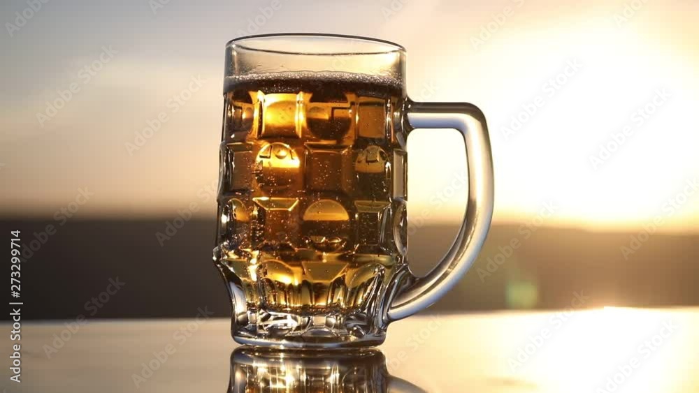 Glass of beer on a beach at sunset. Cooling summer drink concept. Close Up of A Glass of Draught Beer with the Bokeh of Sunlight Background, Soft Focus