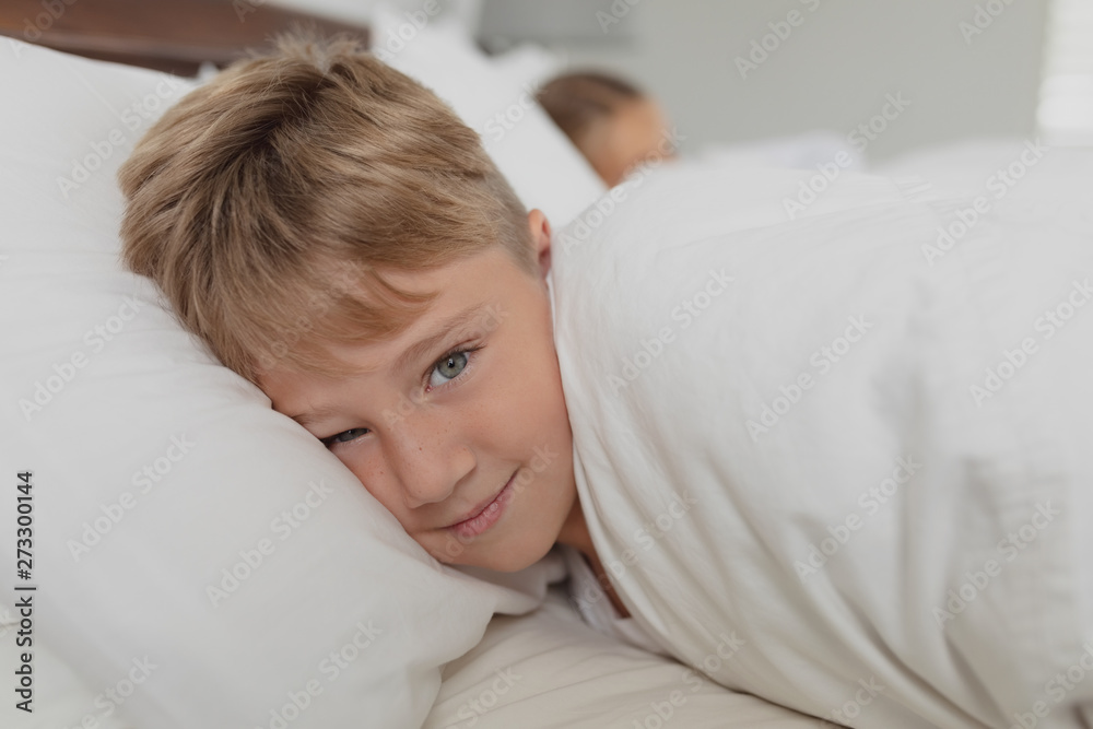 Fototapeta premium Cute boy looking at camera while lying on bed in bedroom at comfortable home