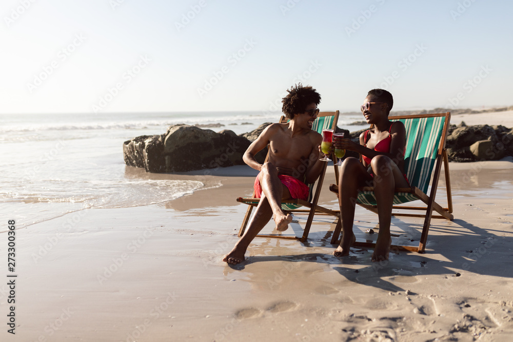 Couple toasting glasses of cocktail while relaxing in a beach chair on the beach