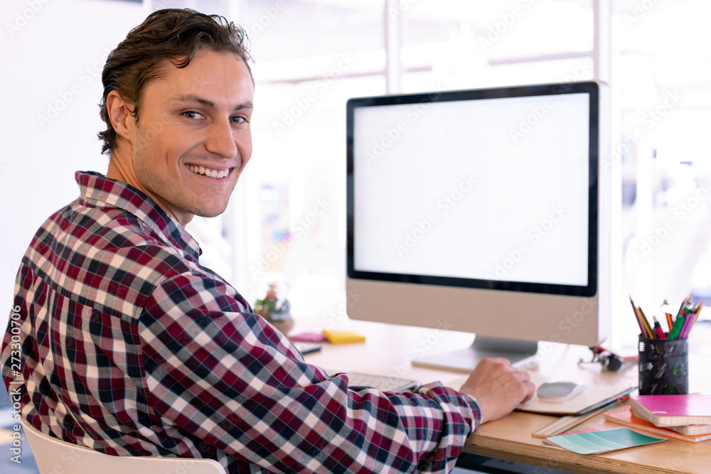 Male graphic designer looking at camera while working on computer at desk in a modern office Male graphic designer looking at camera while working on computer at desk in a modern office