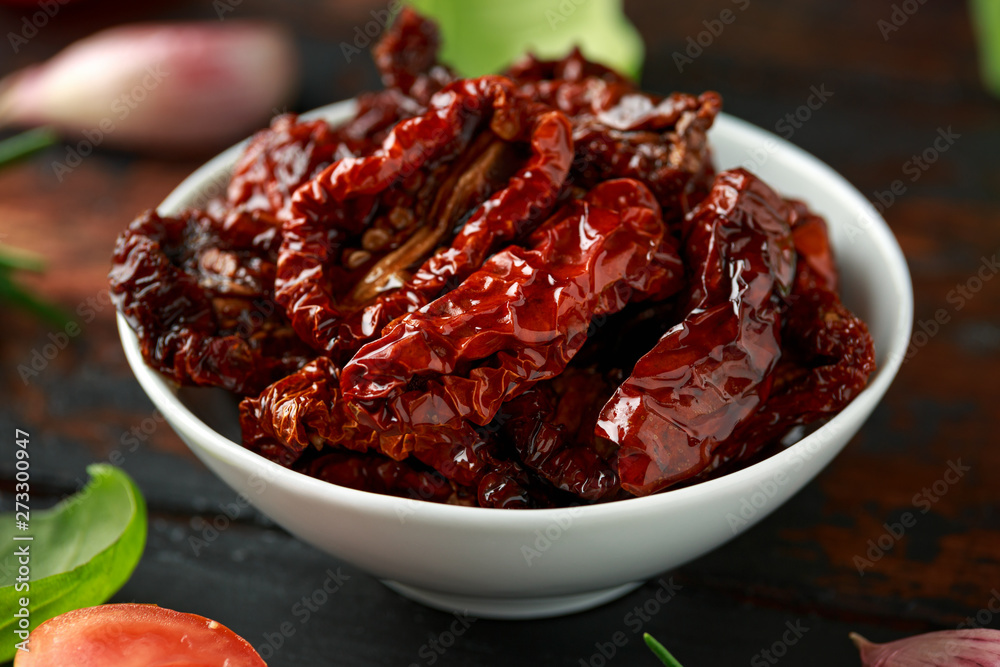 Sun dried tomatoes in white bowl with fresh herbs and spices on wooden table Sun dried tomatoes in white bowl with fresh herbs and spices on wooden table