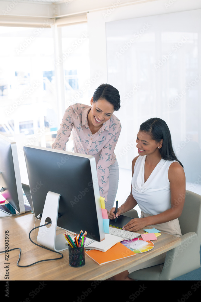 Female graphic designers discussing on computer at desk in a modern office