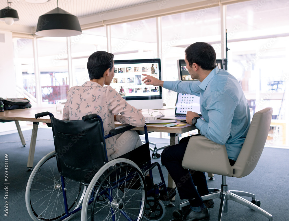 Graphic designers discussing over computer at desk in a modern office Graphic designers discussing over computer at desk in a modern office