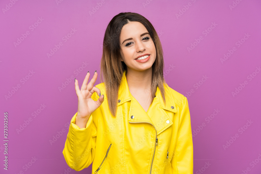 Young woman over purple background showing an ok sign with fingers Young woman over purple background showing an ok sign with fingers