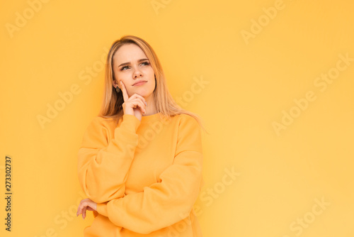 Thoughtful girl in orange clothes looking to the empty place and thinking,on a yellow background, сlose-up portrait. Blonde girl looks out to the empty place and thinks isolated on a yellow background