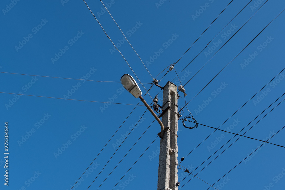 Street lamppost with wires. Concrete pole with a lantern. Street lamp with a bird.