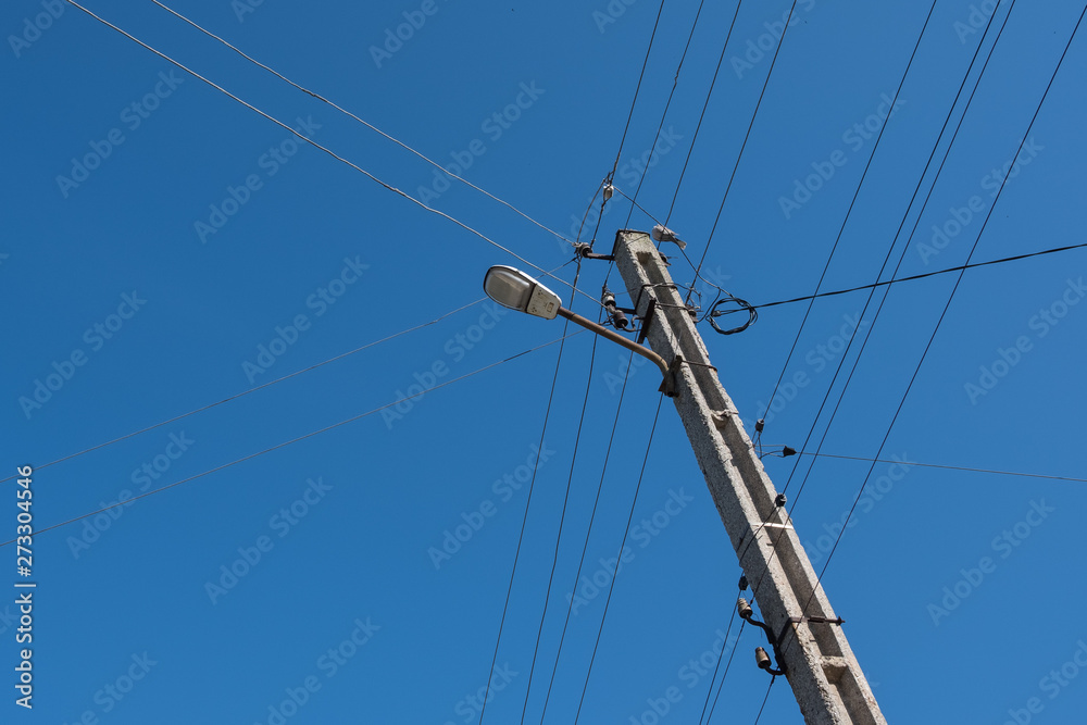 Street lamppost with wires. Concrete pole with a lantern. Street lamp with a bird.