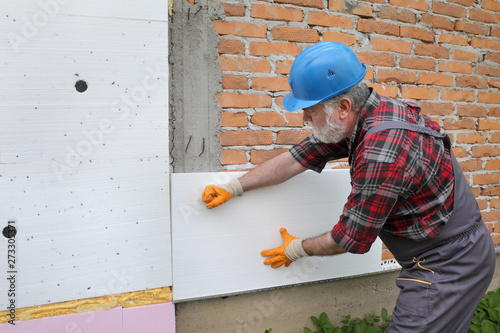 Worker placing styrofoam insulation to brick wall, house renovation