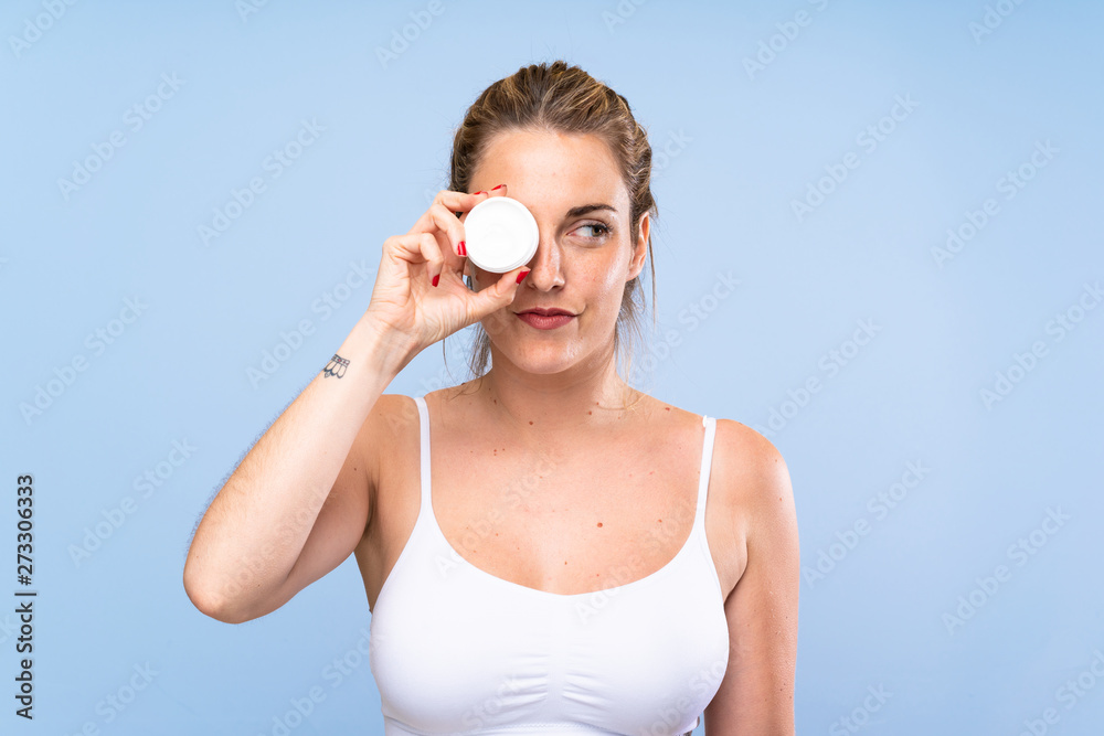 Young blonde woman with moisturizer over isolated blue wall Young blonde woman with moisturizer over isolated blue wall