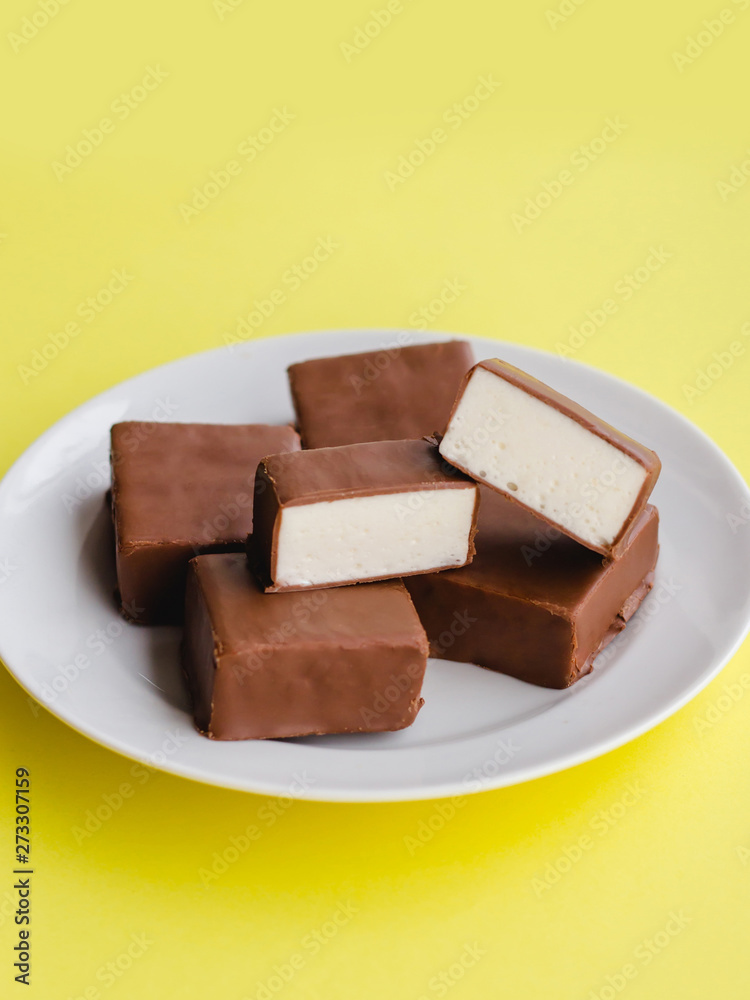 Chocolate sweets with white souffle on a plate on a yellow background. Chocolate sweets with white souffle on a plate on a yellow background.