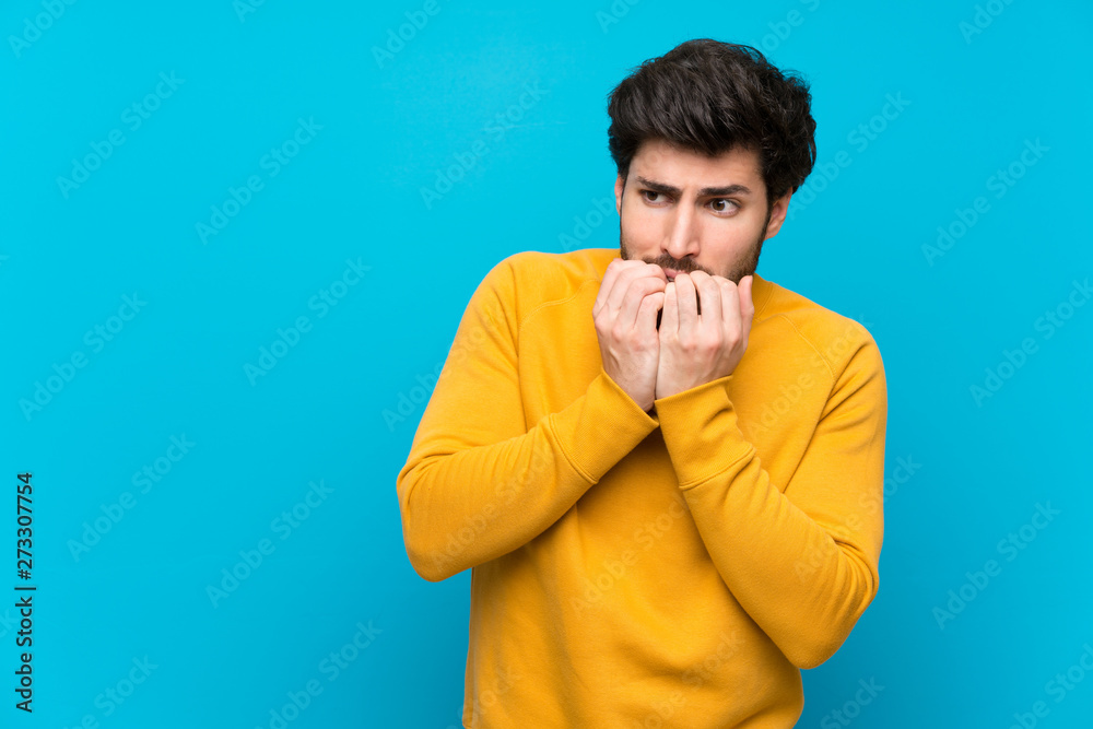 Handsome over isolated blue wall nervous and scared putting hands to mouth Handsome over isolated blue wall nervous and scared putting hands to mouth