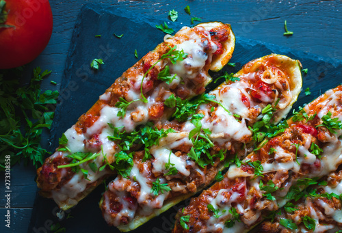 Close-up of stuffed zucchini boats with ground beef, spicy tomato sauce, cheese and fresh parsley, on dark background, top view photo