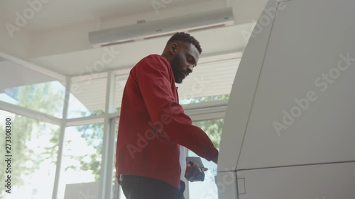 African american attractive man getting money from an ATM cash machine with a credit card inside the bank. photo