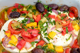 Large portion of ripened Halloumi or Feta cheese with many fresh herbs, tomatoes and red onions in a casserole dish for grilling in the oven or on the grill for a barbecue