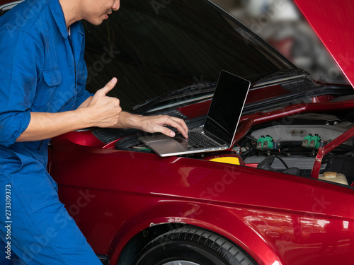 Close up of mechanic hand using laptop computer to check a car engine and showing thumbs up at the repair garage. Auto repair, car service and maintenance concept. © natsarun