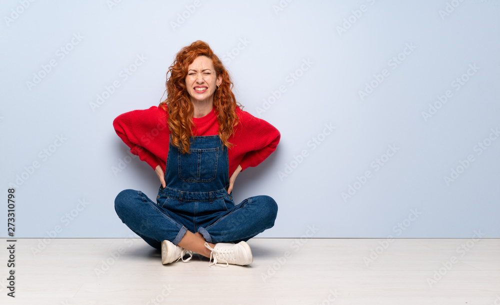 Redhead woman with overalls sitting on the floor suffering from ...