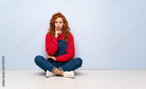 Redhead woman with overalls sitting on the floor Looking front