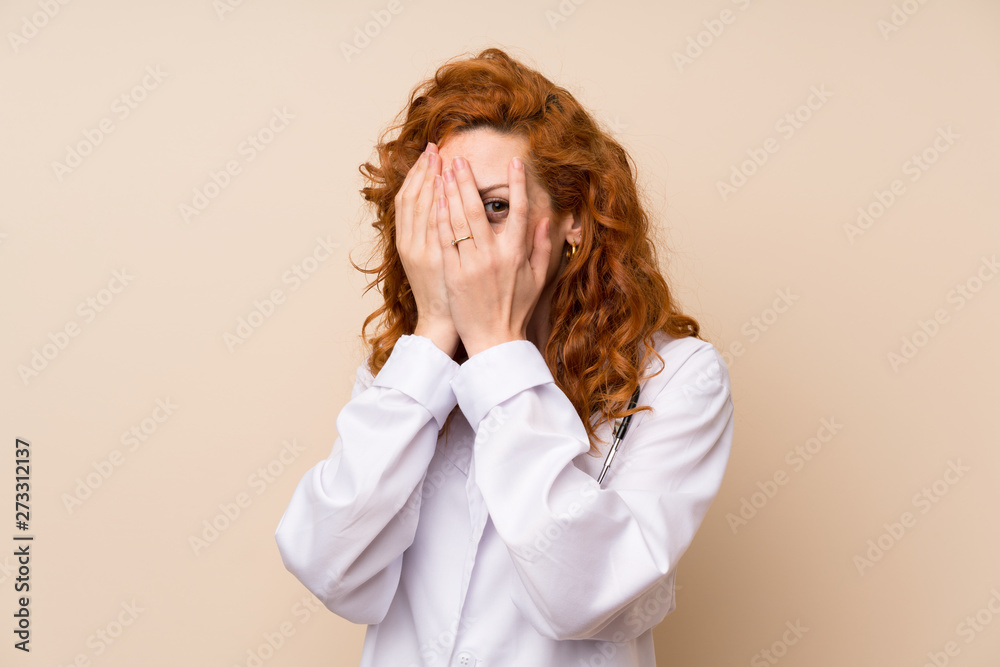 Redhead doctor woman covering eyes and looking through fingers Redhead doctor woman covering eyes and looking through fingers