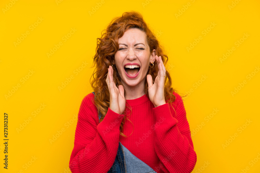 Redhead woman with overalls over isolated yellow wall laughing Redhead woman with overalls over isolated yellow wall laughing