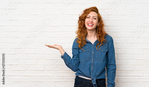 Bild auf Leinwand Redhead woman over white brick wall holding copyspace imaginary on the palm to i