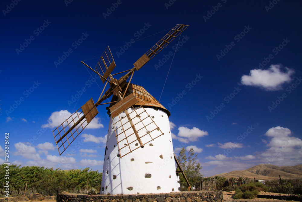 View on isolated ancient white windmill with brown wings against blue sky with few scattered clouds - Fuerteventura, El Cotillo