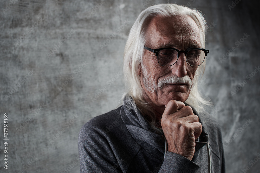 Aged gray haired Caucasian retired man thinking about life. Grandfather in glasses with mustache and thoughtful facial expression holds his chin