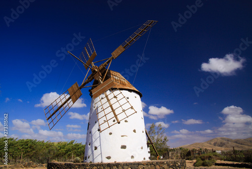 View on isolated ancient white windmill with brown wings against blue sky with few scattered clouds - Fuerteventura, El Cotillo