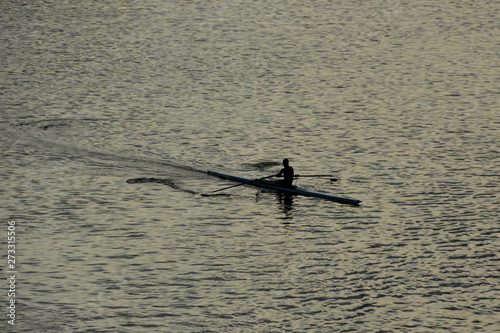 Single rower silhouette rowing into the sunrise on the river