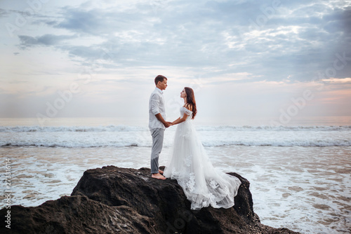 Elegant gorgeous bride and groom walking on ocean beach during sunset time. Romantic walk newlyweds on tropical island. Concept marriage, just married