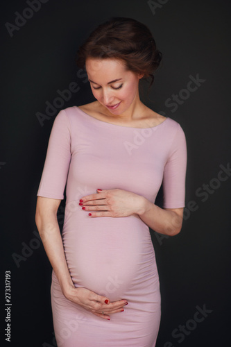 Pregnant happy Woman touching her belly. Pregnant middle aged mother portrait, caressing her belly and smiling close-up. Healthy Pregnancy concept, brunette expectant female on blue background photo