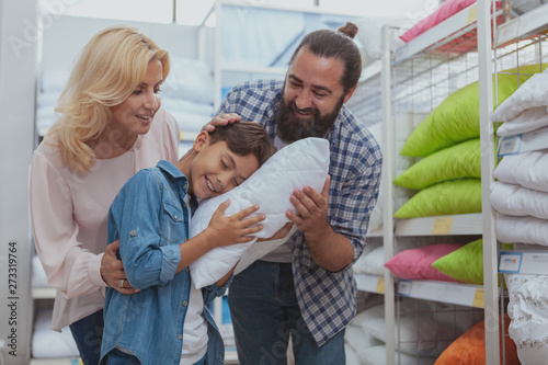 Loving parents buying orthopedic pillow for their lovely young son. Happy family shopping at home goods store. Adorable boy trying comfortable pillow at furnishings shop with his parents